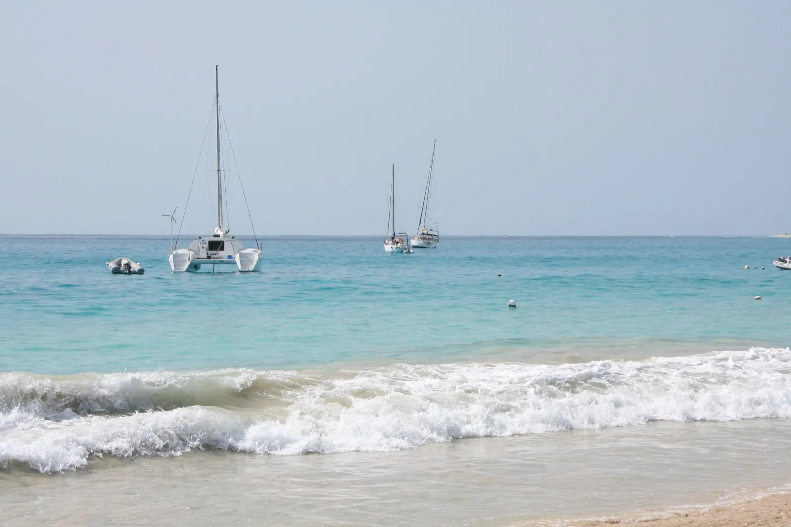 Türkisfarbene Untiefen am Strand von Santa Maria auf Sal mit einem Katamaran und Yachten vor Anker