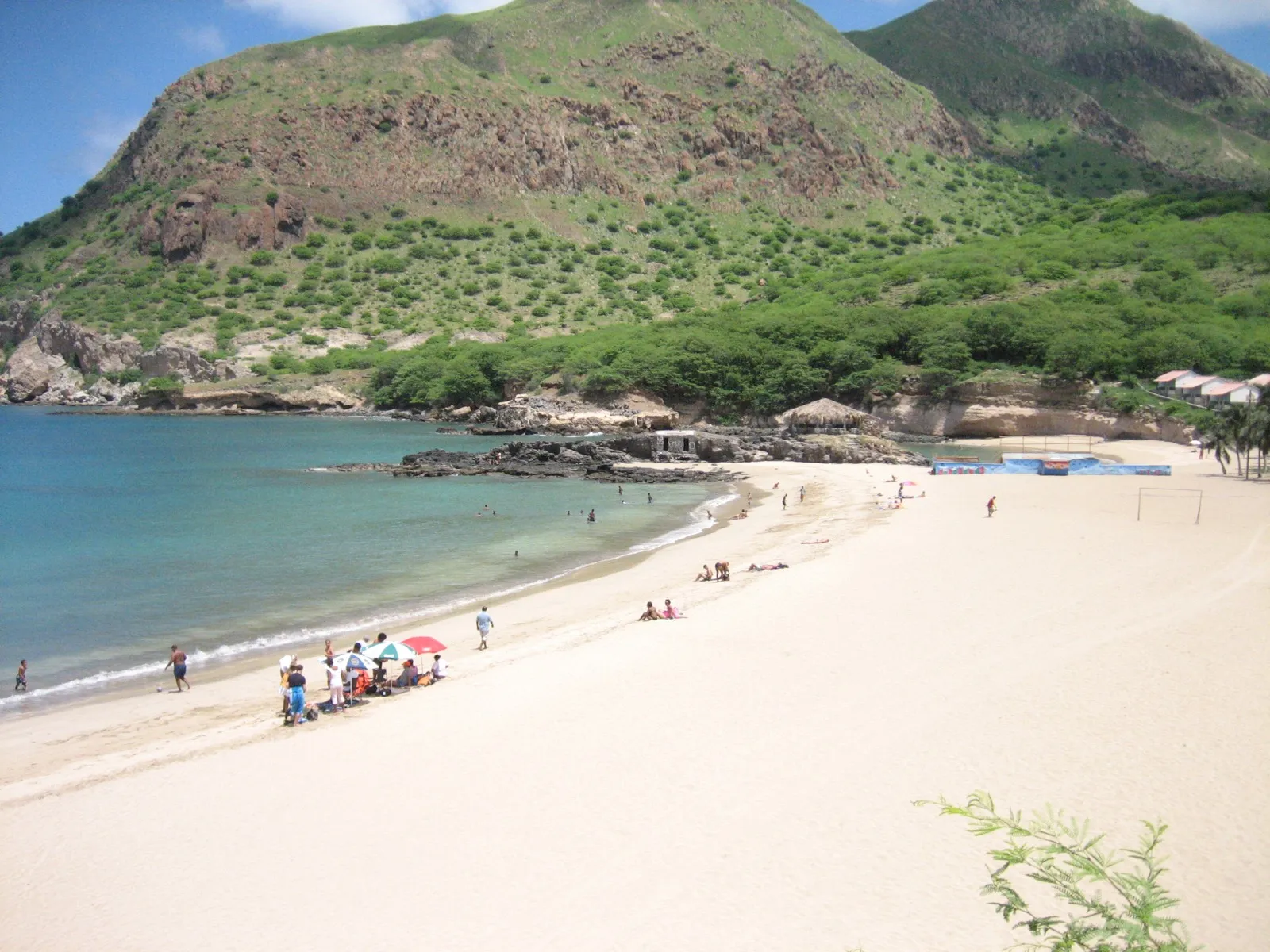Weißer Sand und türkisfarbenes Wasser der Bucht von Tarrafal unter einer grünen vulkanischen Landzunge im Norden von Santiago